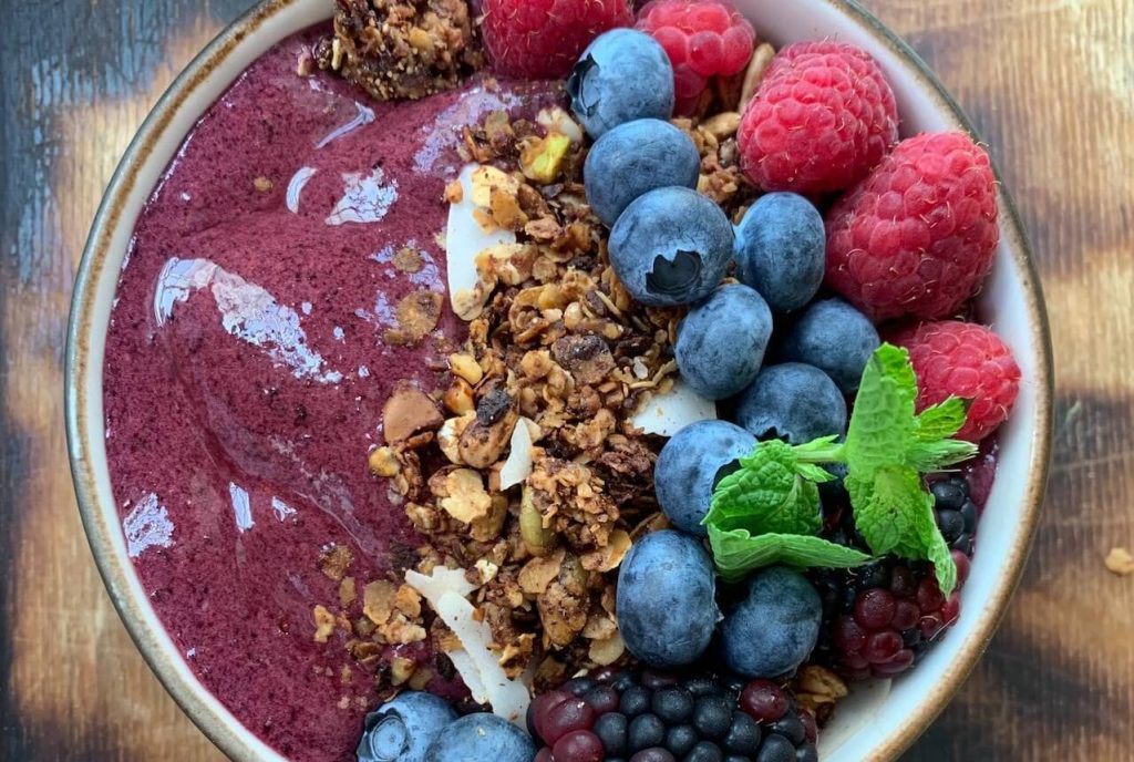 A vibrant and refreshing acai bowl, featuring a thick and smooth blend of frozen acai berries, topped with granola, sliced fruits, coconut flakes, and a drizzle of honey. 